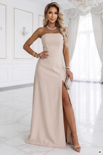 Modelis prezentē gaiši bēšu Numoco maxi kleitu bez bretellēm ar augstu šķēlumu - elegantu vakara kleitu minimālistiskā interjerā.}