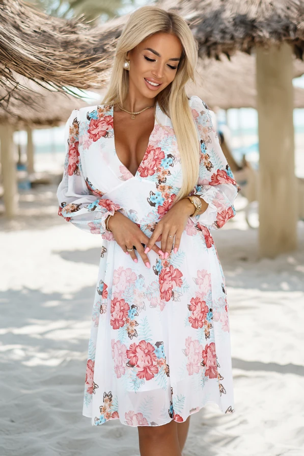 Modelka prezentuje zwiewną kopertową sukienkę w kwiaty z długim, transparentnym rękawem i głębokim dekoltem; lekka, romantyczna stylizacja idealna na wiosnę i lato, produkt polski marki Numoco.